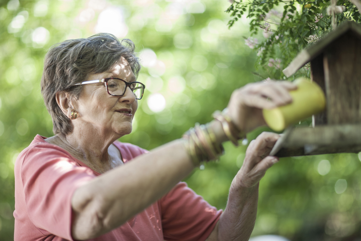 elderly lady putting birdseed in birdfeeder